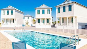 Una piscina con una valla blanca y tres edificios blancos al fondo.