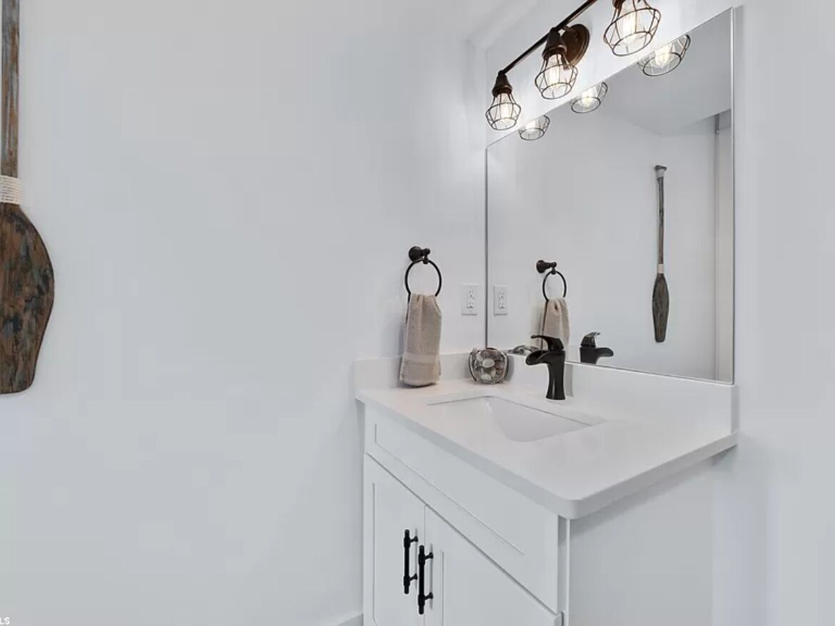 Un baño moderno con tocador blanco, un espejo grande y una lámpara sobre el espejo.