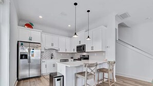 Una cocina moderna con gabinetes blancos, electrodomésticos de acero inoxidable y una isla central con taburetes.