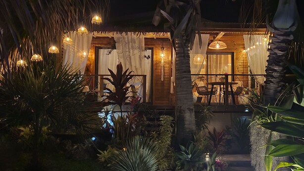 A wooden house with a balcony, surrounded by tropical plants and string lights. - Bungalow Pour 2 Personnes Ti Kaz Paradis (Le Tampon)