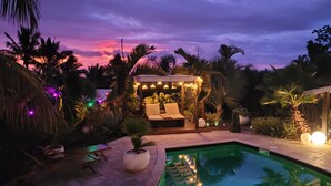 A pool area with lounge chairs, a covered seating area with string lights, and a small waterfall feature. - Bungalow Pour 2 Personnes Ti Kaz Paradis (Le Tampon)