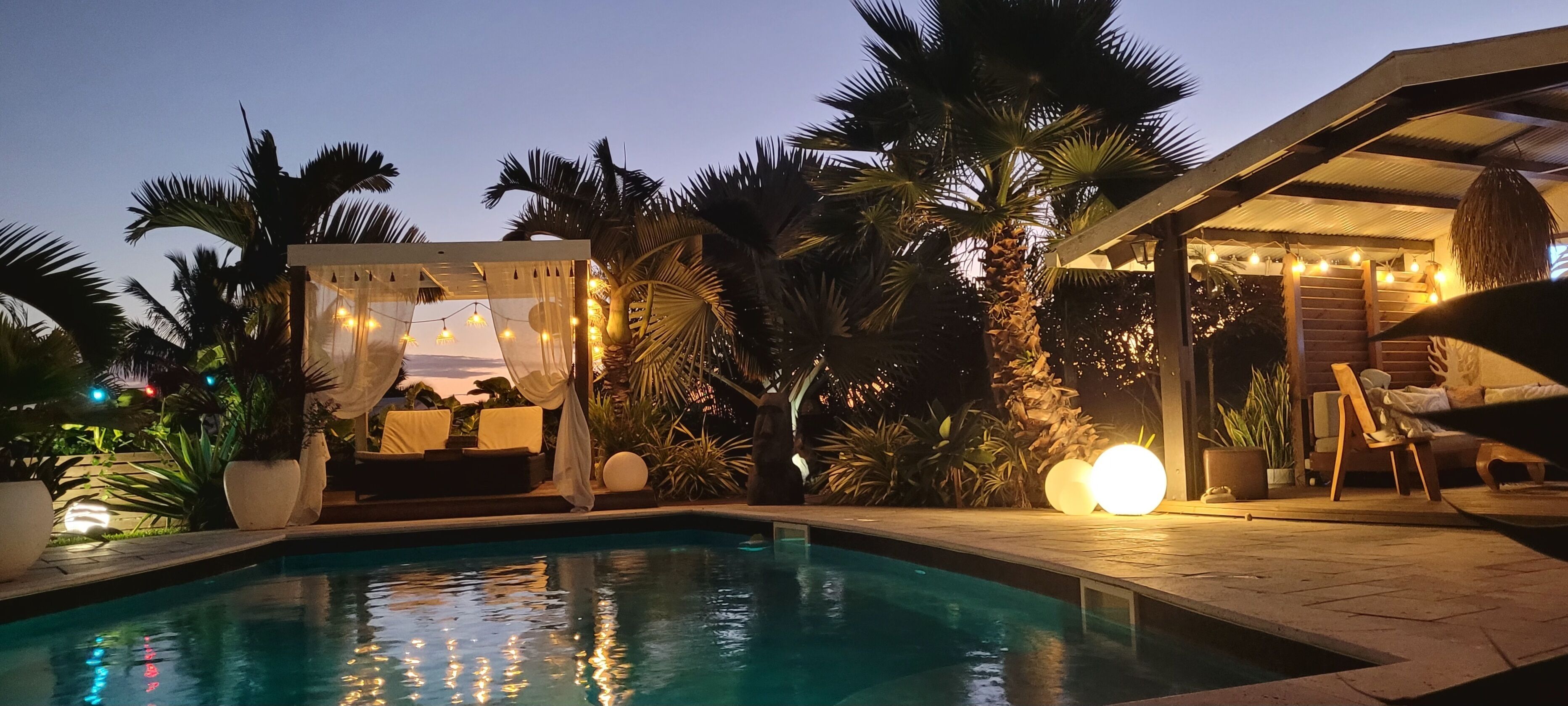 A swimming pool with a covered seating area and palm trees.