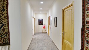 Un corridoio stretto con un tappeto decorativo a sinistra, una sedia rossa al centro e una porta in legno a destra.