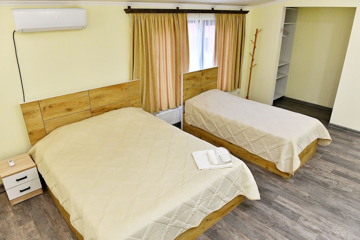 Quarto de hotel com duas camas de solteiro, cabeceira de madeira, mesa de cabeceira com abajur e guarda-roupa.