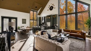A spacious living area with a high ceiling, large windows, and a modern kitchen. - Spacious 4BR|Indoor Pool|Hot Tub|Games|Fire Pit (Sevierville)