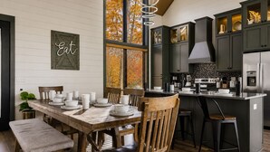 A modern kitchen with a wooden dining table set for four, a built-in island, and dark cabinetry. - Spacious 4BR|Indoor Pool|Hot Tub|Games|Fire Pit (Sevierville)