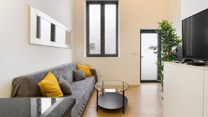 Un salón moderno con un sofá gris, cojines amarillos, una mesa de centro de cristal, un televisor de pantalla plana y una planta en maceta.