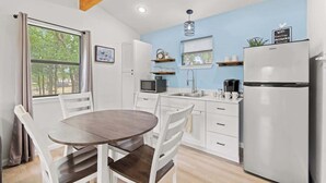 Cocina compacta con muebles blancos, refrigerador, microondas y comedor con una mesa redonda y sillas.