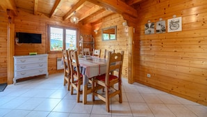 A wooden cabin interior with a dining table, chairs, a TV, and a window. - “Our Chalet” with Mountain View, Private Terrace and Wi-Fi (vecoux)