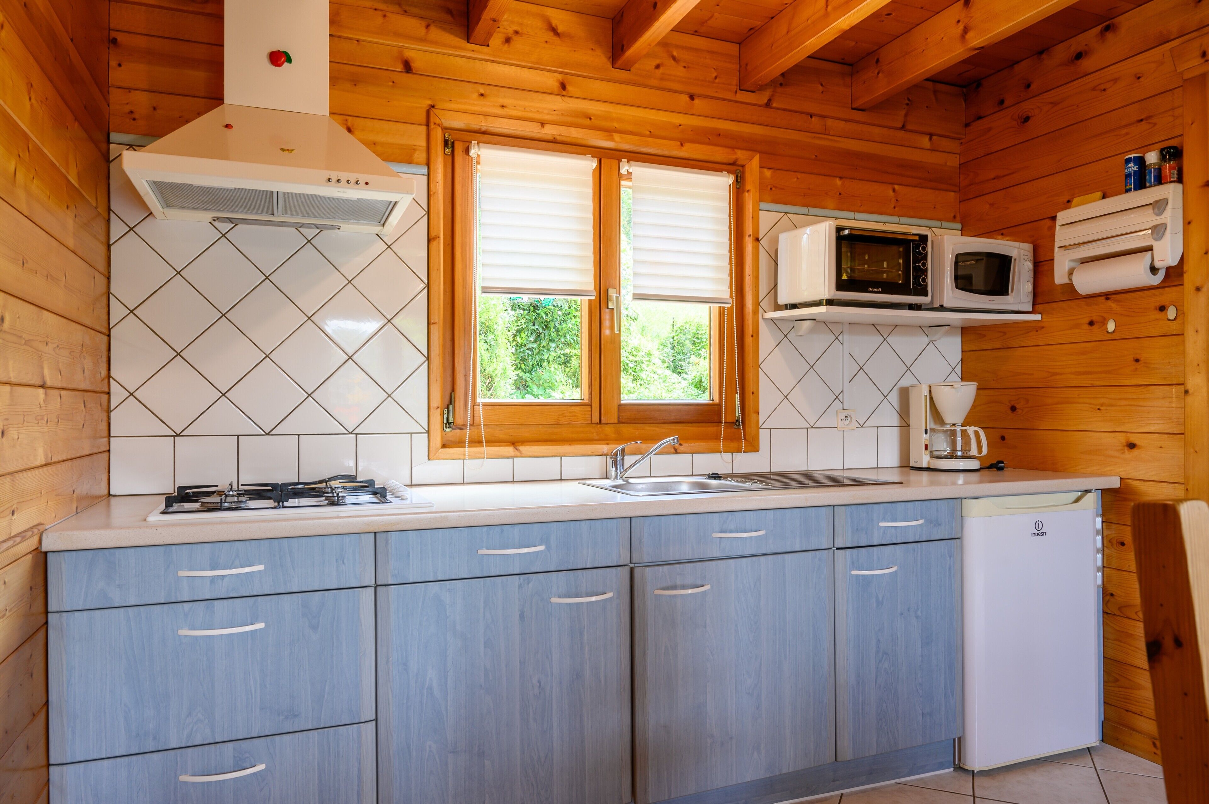 Una cocina con paredes de madera, una estufa a gas, un microondas, un lavamanos y armarios.