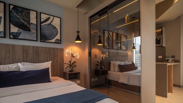 Una habitación de hotel moderna con una cama grande, una zona de descanso separada, una kitchenette y obras de arte en las paredes.
