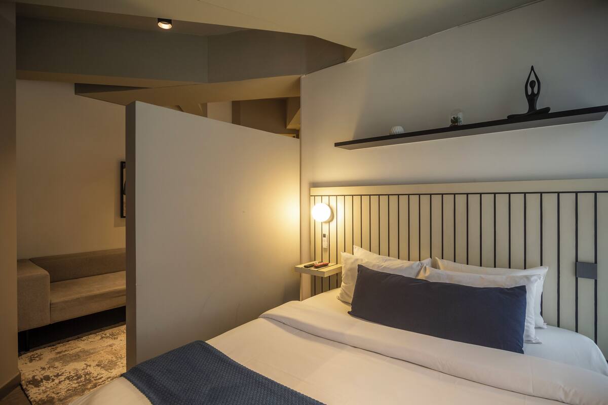 A modern hotel room with a large bed, a nightstand, a wall-mounted shelf, and a staircase leading to an upper level.