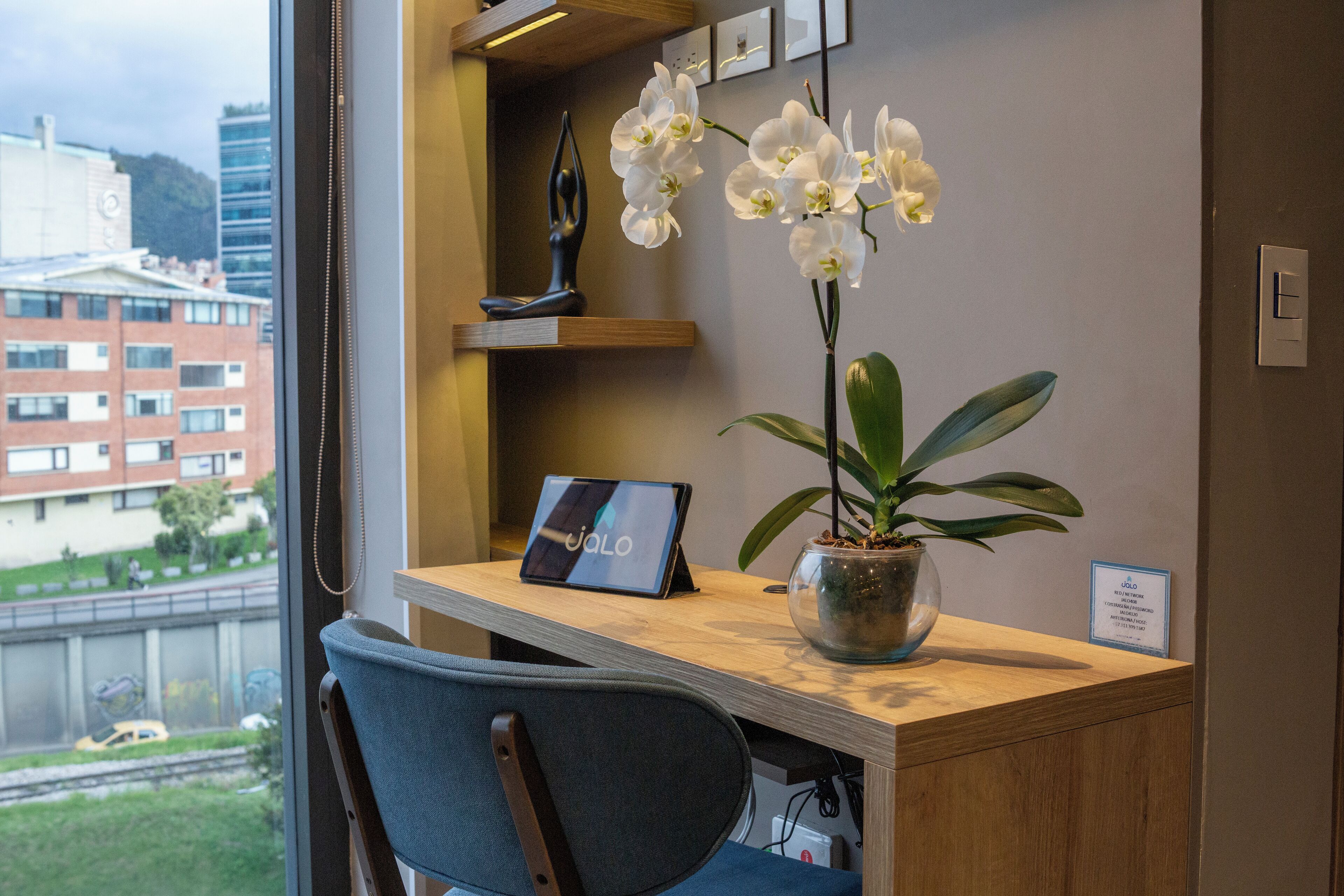 A desk with a laptop, a potted plant, and a vase with white orchids.