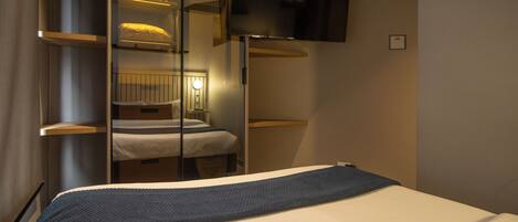 A modern hotel room with a bed, a television mounted on the wall, and a mirror reflecting the room's interior.