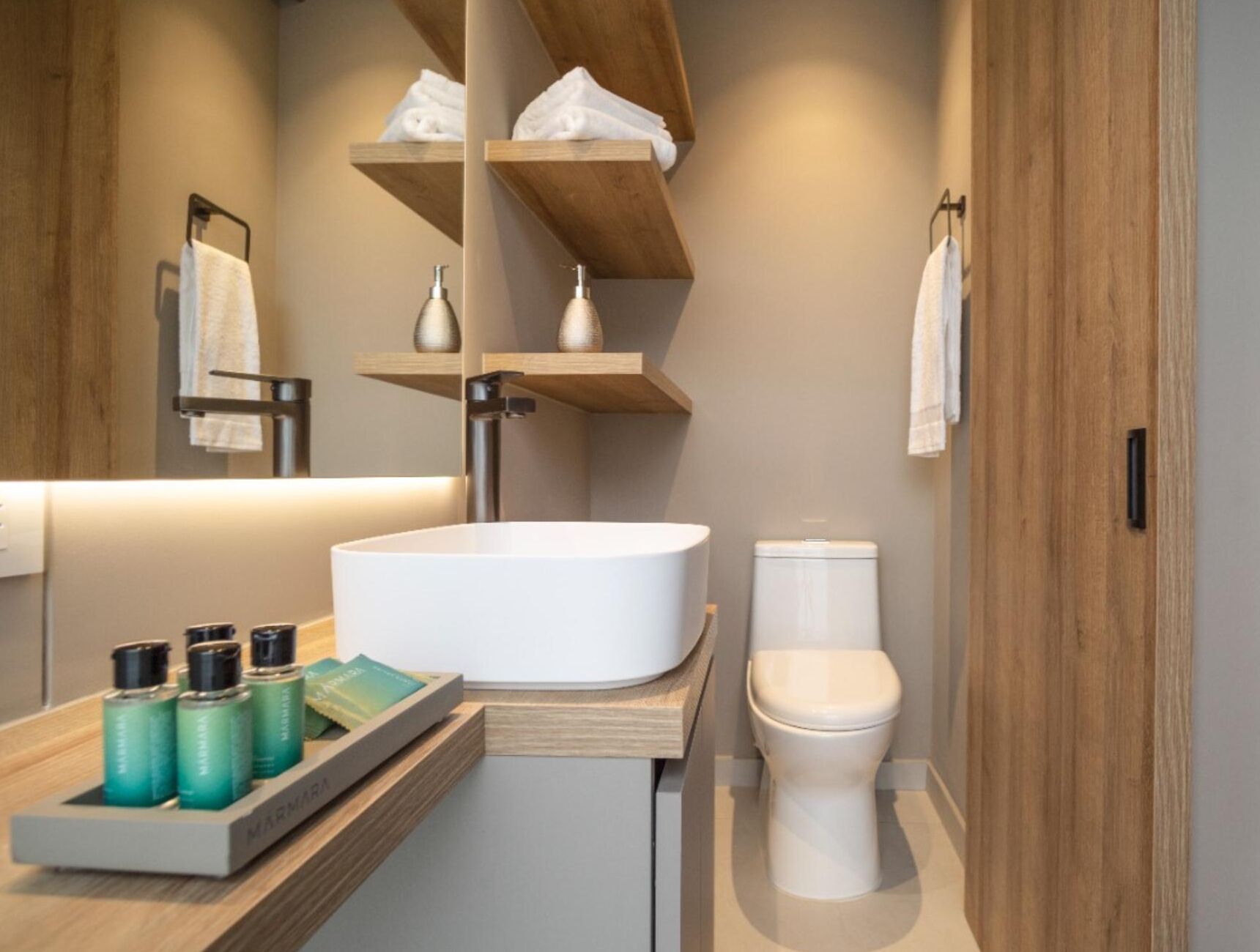 Un baño moderno con lavamanos independiente, inodoro y estanterías de madera con toallas.