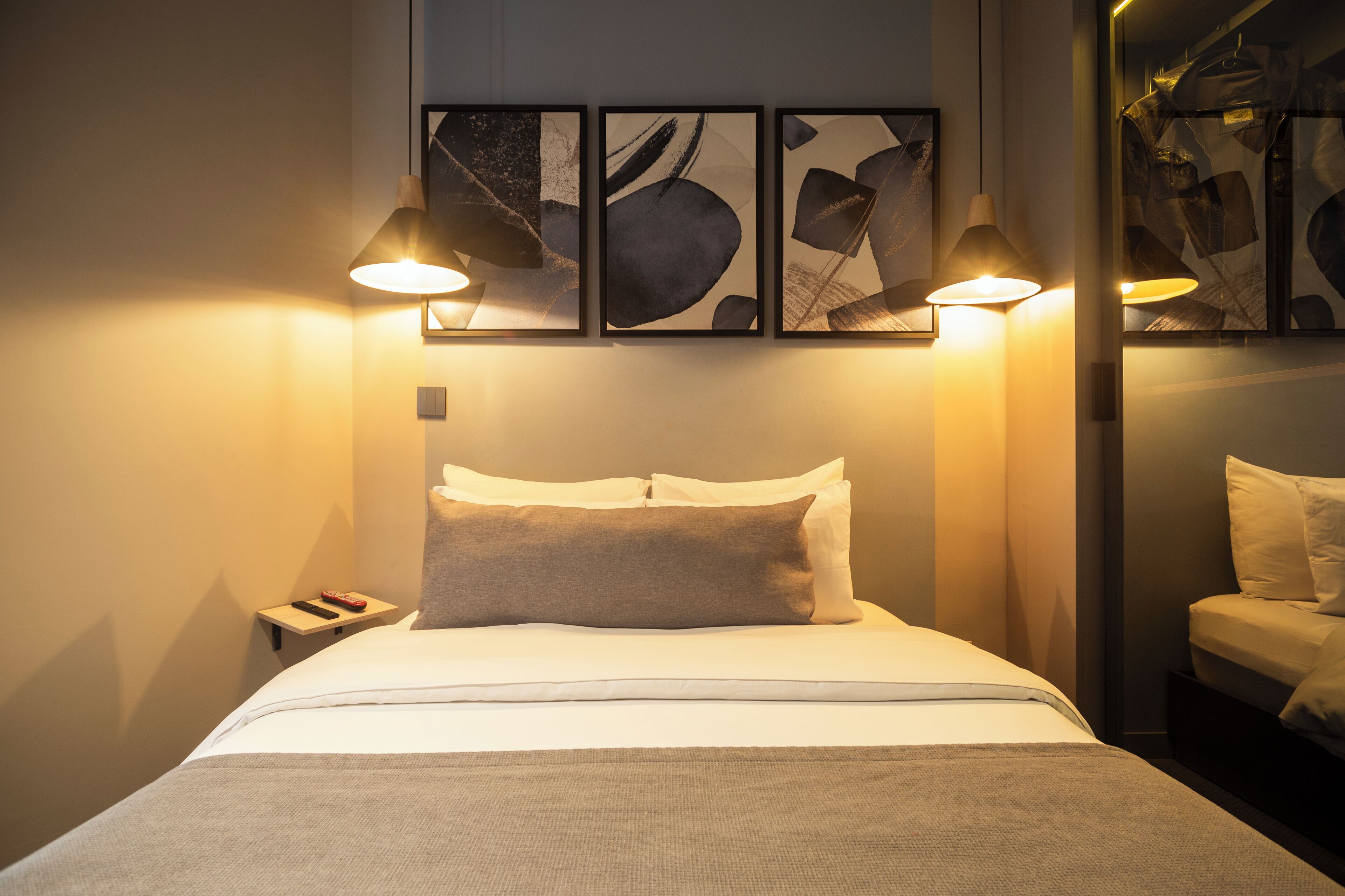 A hotel room with a bed, two bedside lamps, a nightstand, and abstract artwork on the wall.
