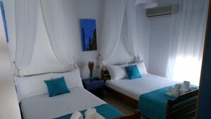 Een hotelkamer met twee bedden, elk met een blauwe spreideken en kussens, een nachtkastje met een vaas en een schilderij aan de muur.
