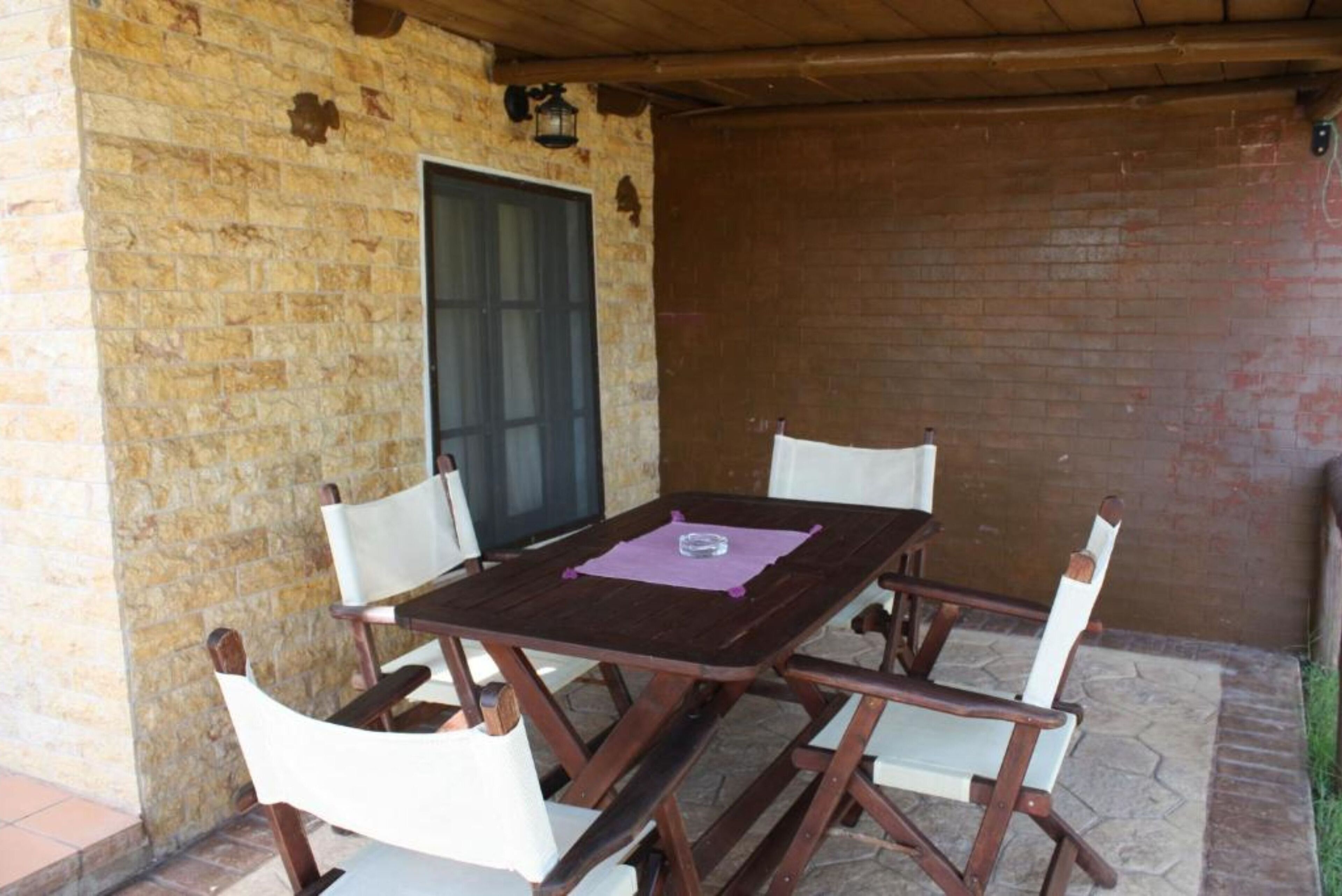 Una mesa de madera con cuatro sillas, un mantel individual morado y una ventana con marco oscuro.