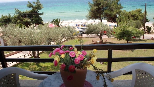 Een balkon met een bloempot, uitzicht op zee, en een strand met parasols.