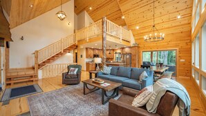 A spacious wooden cabin interior with a living area, kitchen, and a loft bedroom with a balcony. - Cozy Log Chalet Near Wisp w/ Hot Tub (McHenry)