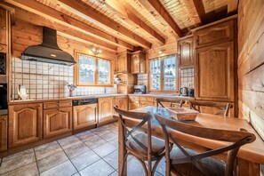 Una cucina in stile baita con elementi in legno, piastrelle a parete, pensili in legno, un grande fornello e un tavolo con sedie.