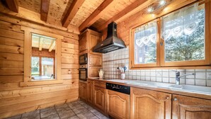 Une cuisine rustique, située dans une cabane en bois, équipée d’un lave-vaisselle, d’une cuisinière et de grandes fenêtres.