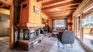 L’intérieur d’une cabane en rondins, avec une cheminée en pierre, des poutres en bois, un canapé et une grande fenêtre.