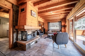 Ein Blockhaus-Interieur mit Kamin aus Stein, Holzbalken, einer Couch und einem großen Fenster.