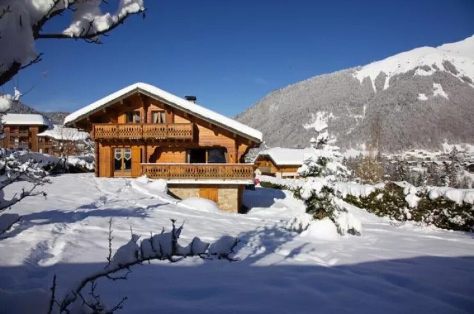 A wooden chalet with a balcony, surrounded by snow-covered landscape and mountains.
