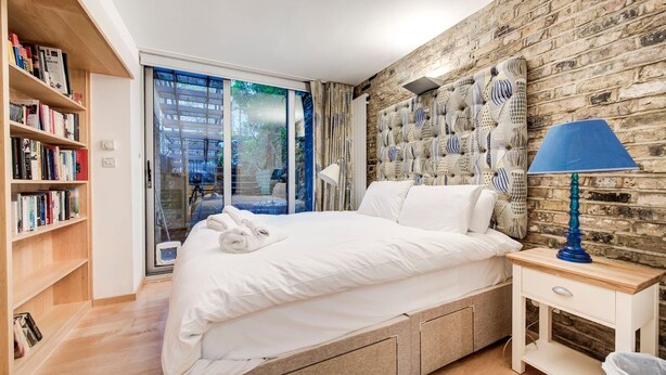 Camera da letto moderna con un letto grande, una libreria in legno, una lampada blu e un muro con motivo a mattoni.