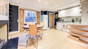 Una cucina moderna con mobili bianchi, un'area pranzo con un tavolo rotondo e sedie, e una vista attraverso una finestra.