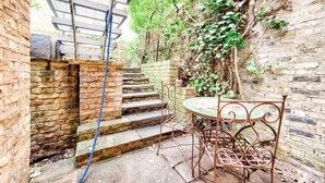 Un'area esterna rustica con un tavolo e una sedia in metallo, un muro in mattoni e una scala in legno.