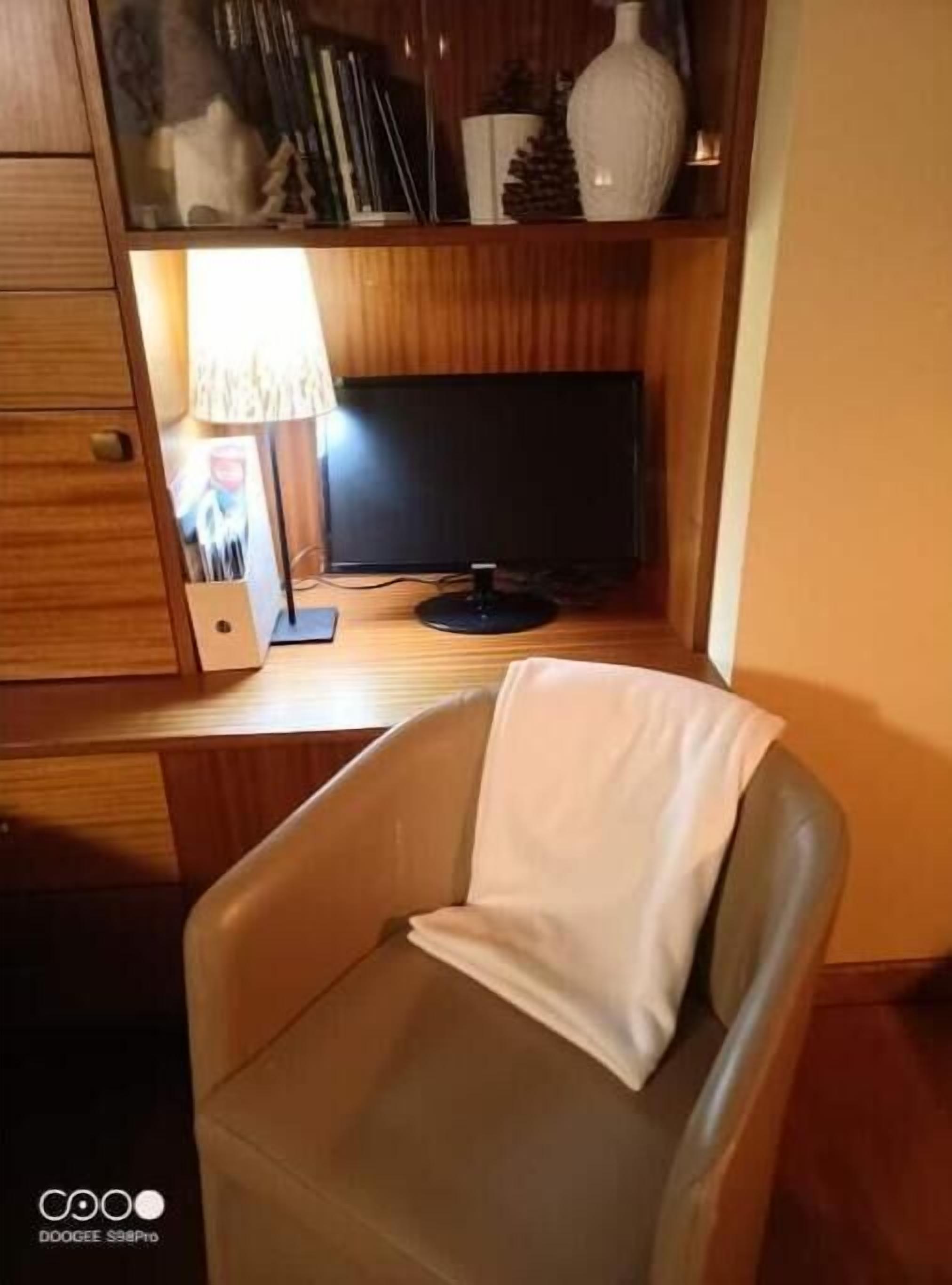 A wooden desk with a computer monitor, a lamp, and a chair.