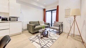 Een moderne woonkamer met een bank, fauteuil, salontafel en een staande ventilator.
