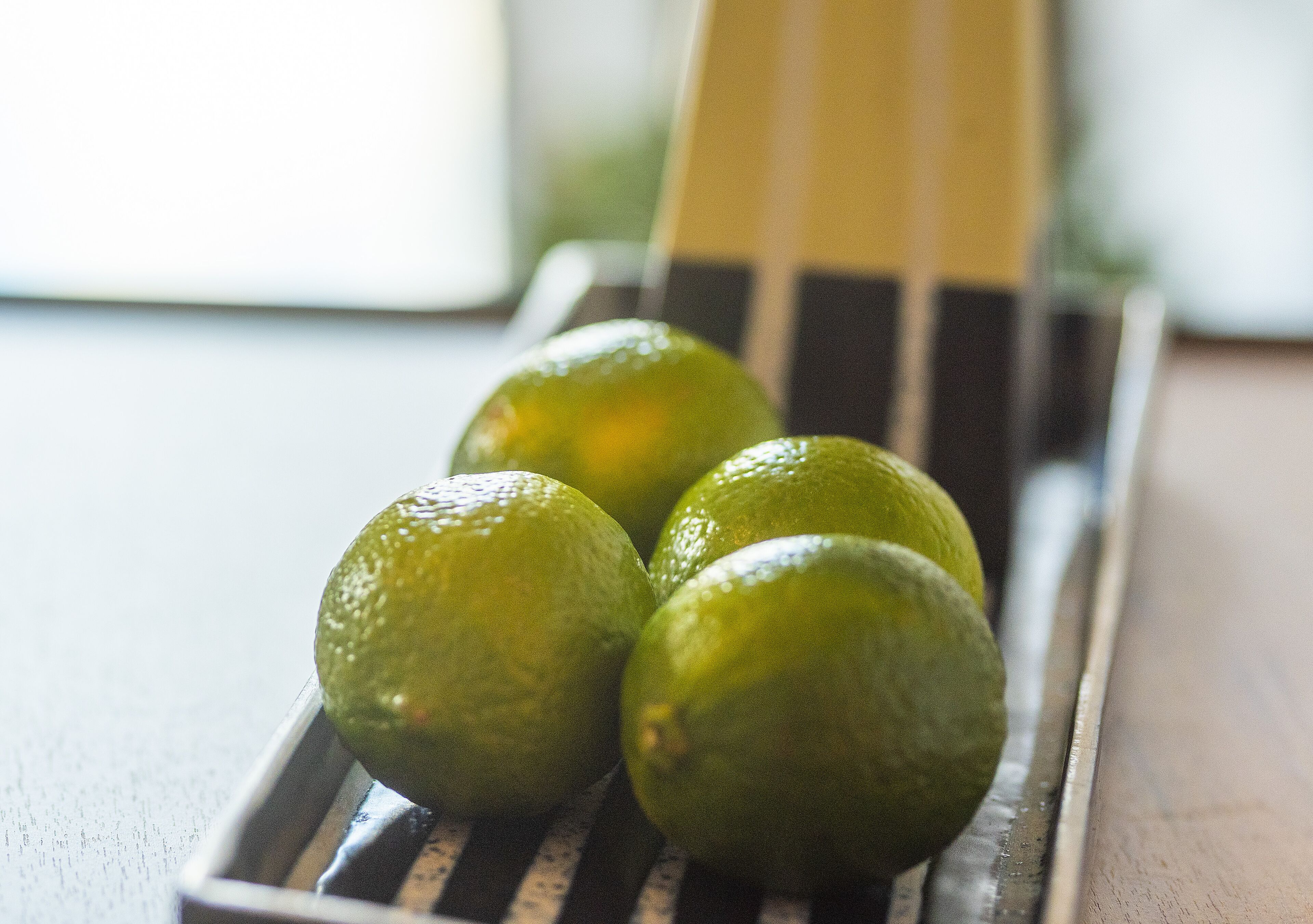 Three limes in a metal tray on a wooden surface.