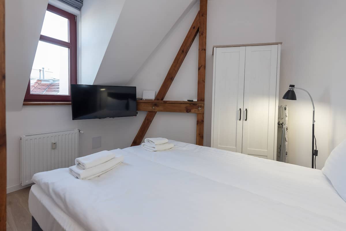Une chambre à coucher comprenant un lit, un téléviseur fixé au mur, une armoire et un radiateur.