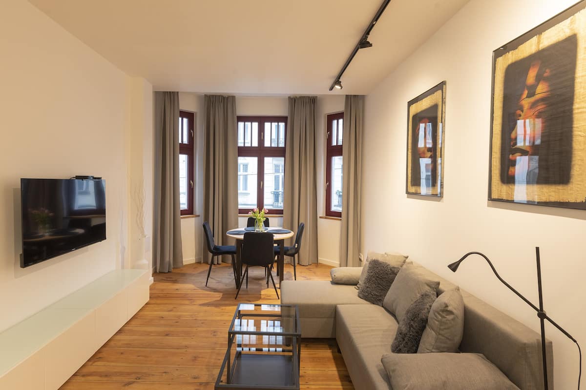 Ein modernes Wohnzimmer mit Flachbildfernseher, einer Couch, einem Couchtisch und einem Essbereich mit Tisch und Stühlen.