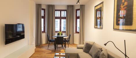 A modern living room with a flat-screen TV, a sofa, a coffee table, and a dining area with a table and chairs.