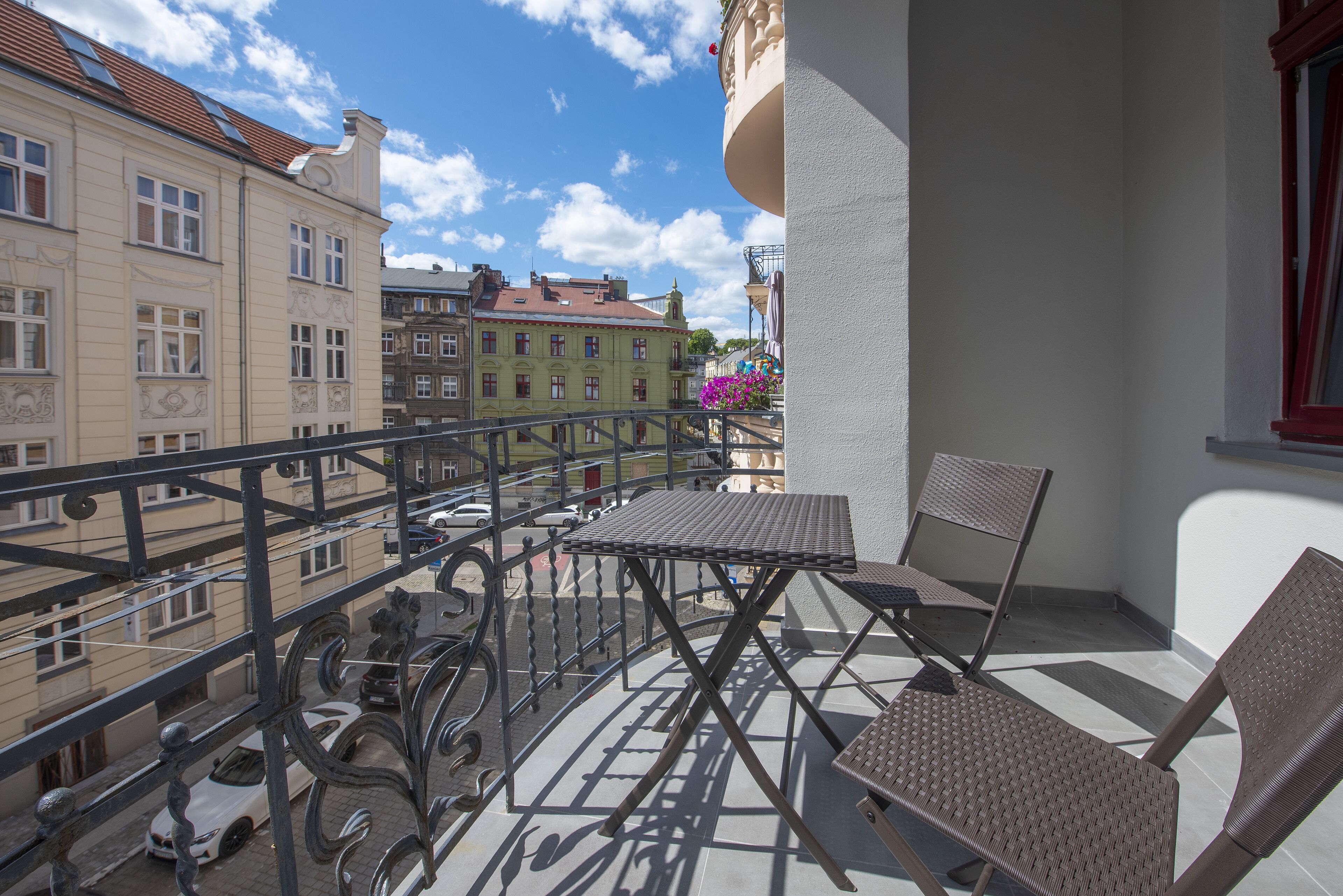 A balcony with a table and chairs, a railing, and a view of buildings and a clear sky.