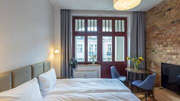 Ein Hotelzimmer mit einem großen Bett, einem Fernseher, einem kleinen Tisch mit Stühlen und einem Fenster mit Blick auf Gebäude.