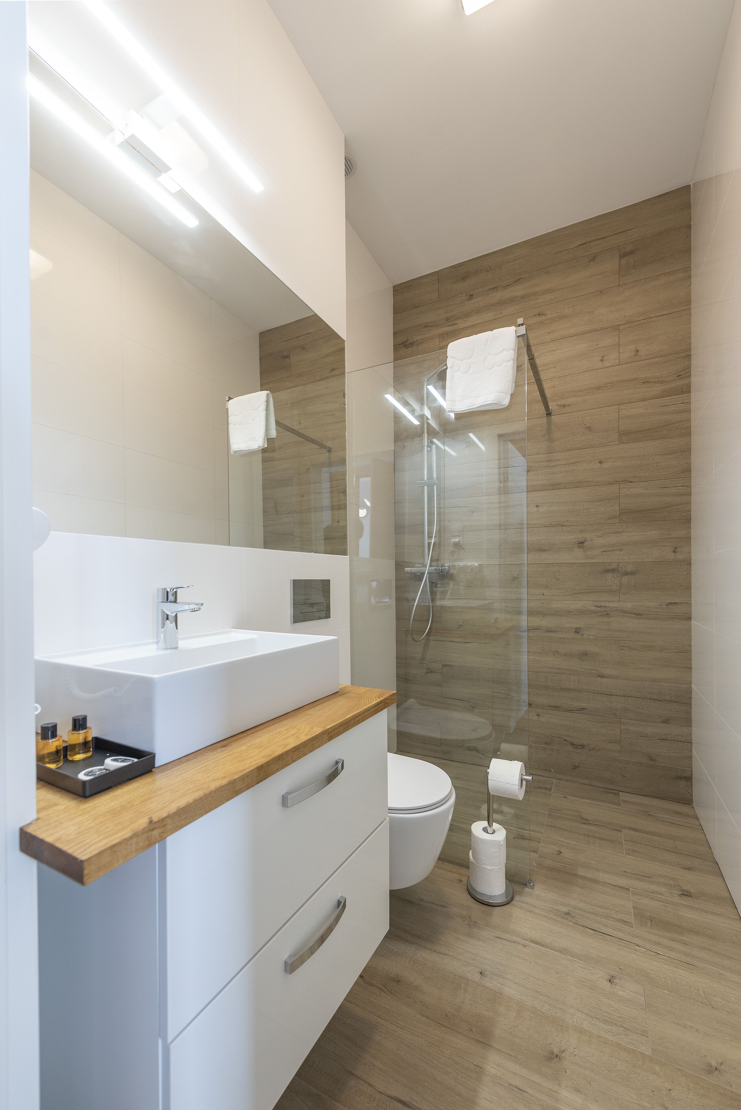 A modern bathroom with a wooden floor, a white sink, and a glass shower enclosure.