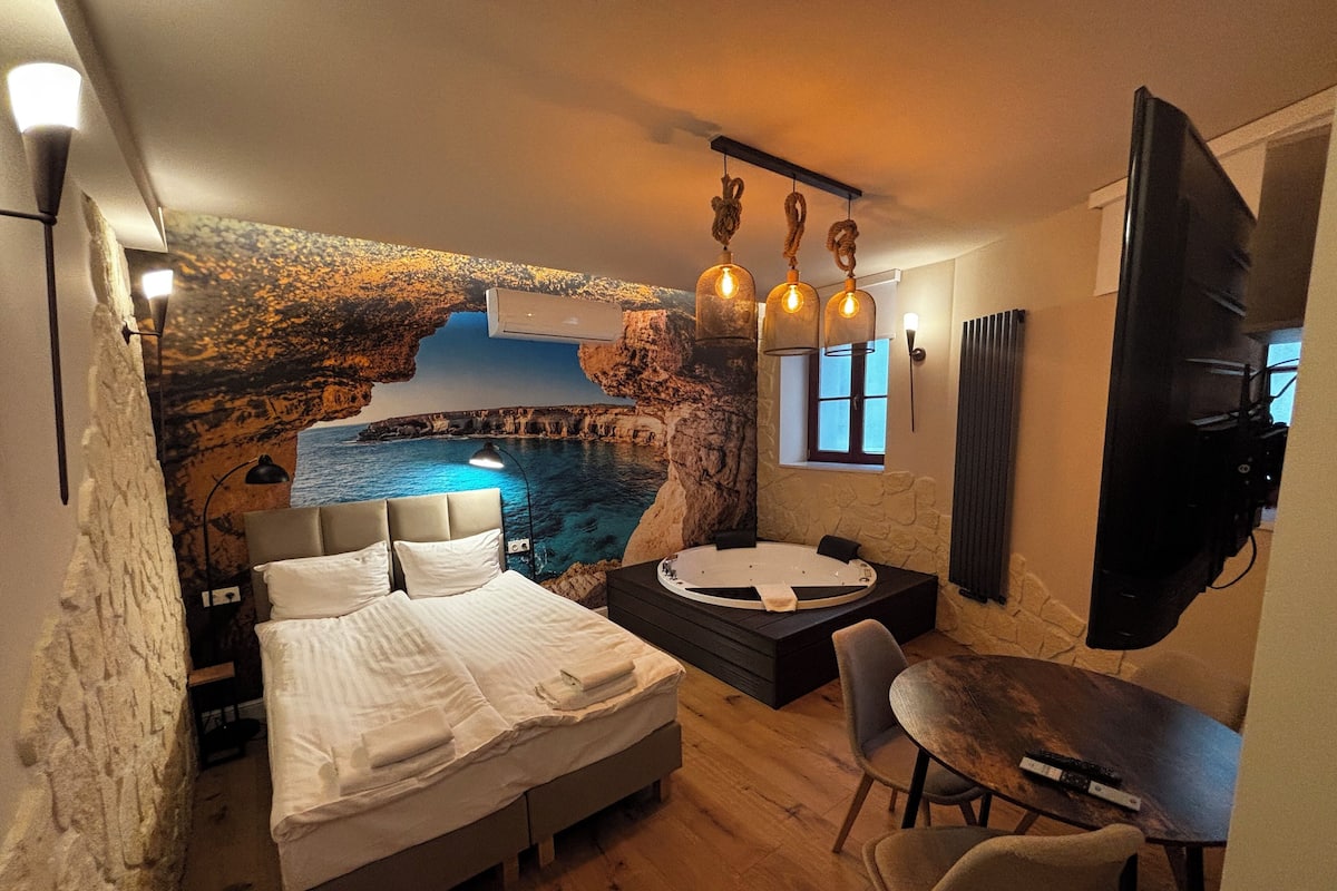 Ein Schlafzimmer mit Bett, einem kleinen Tisch, einem Sessel, einer Badewanne und einem Fernseher.