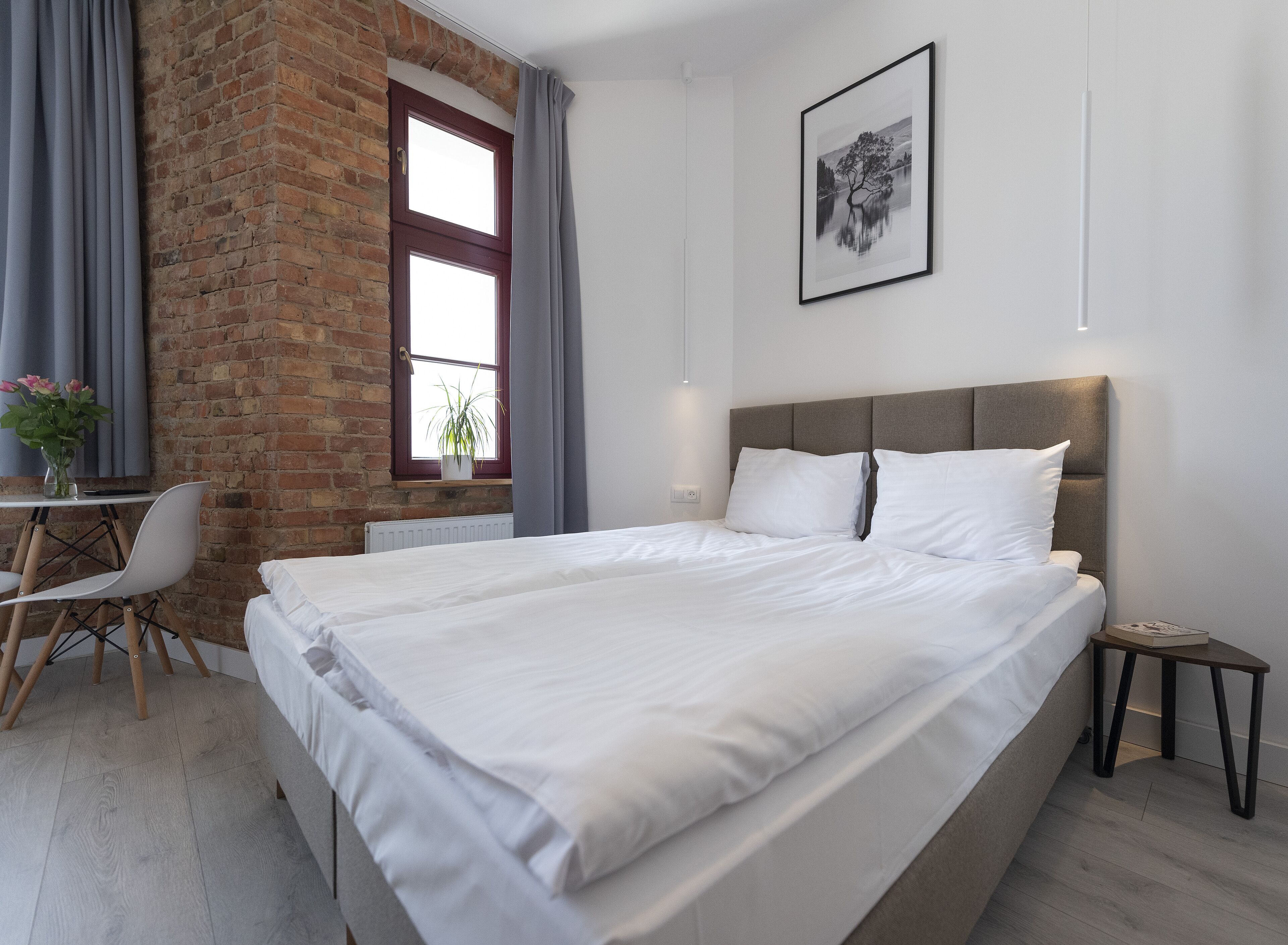 Una camera da letto moderna con un letto grande, una scrivania con una sedia, una pianta in vaso e una finestra con tende.