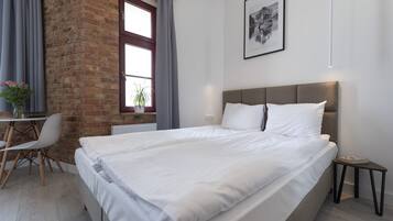 Una camera da letto moderna con un letto grande, una scrivania con una sedia, una pianta in vaso e una finestra con tende.