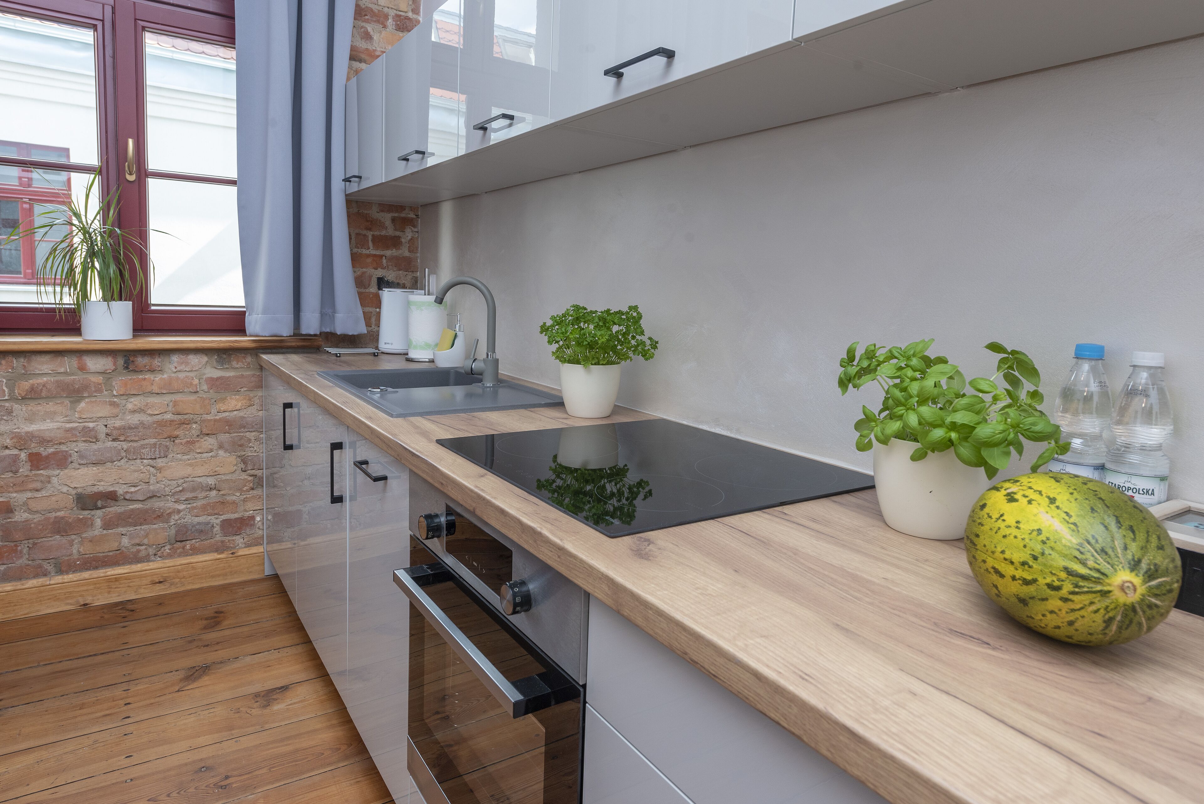 Una cocina moderna con encimera de madera, estufa integrada, fregadero y plantas en macetas.