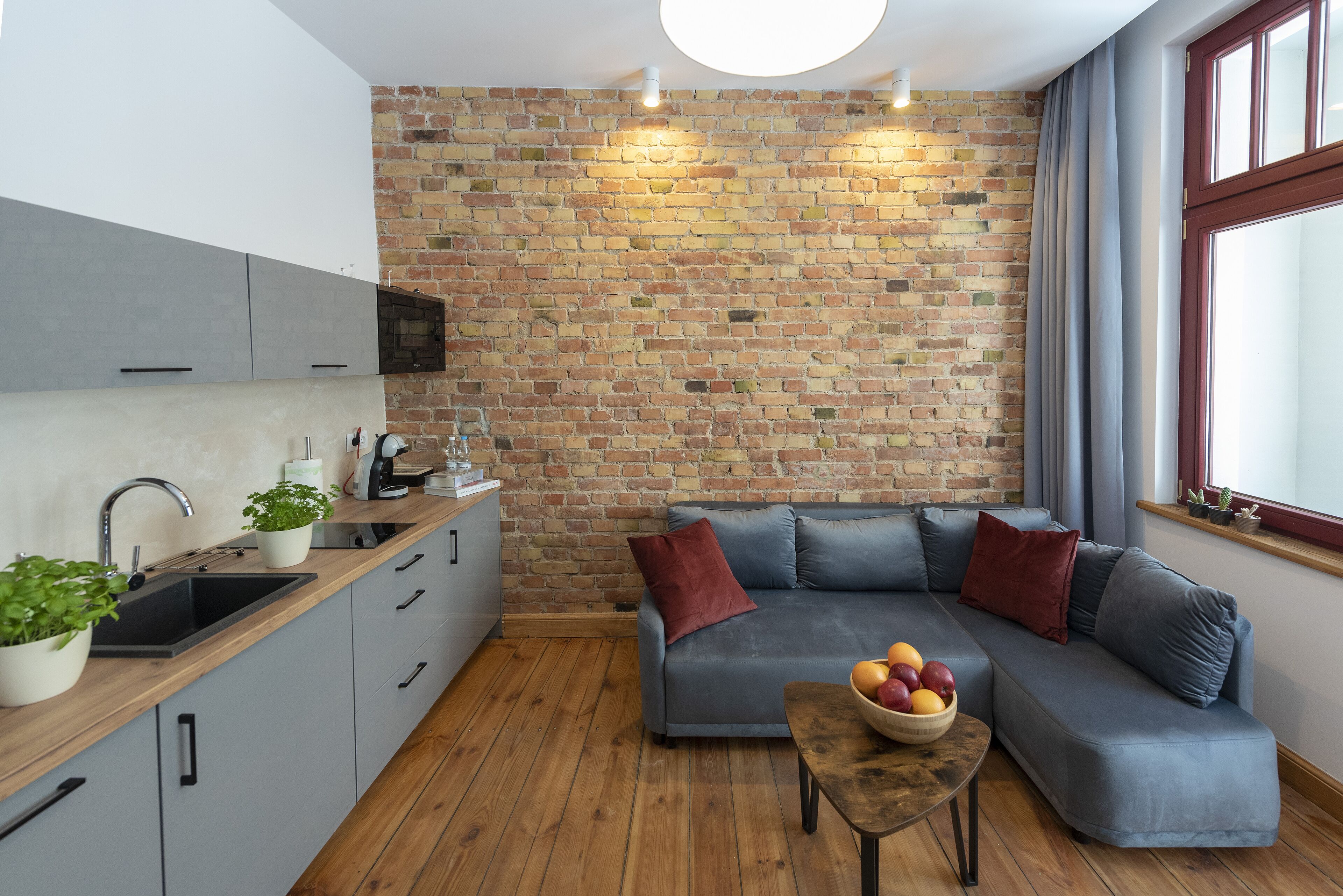 Una cocina moderna con pared de ladrillo, armarios grises y encimera de madera.