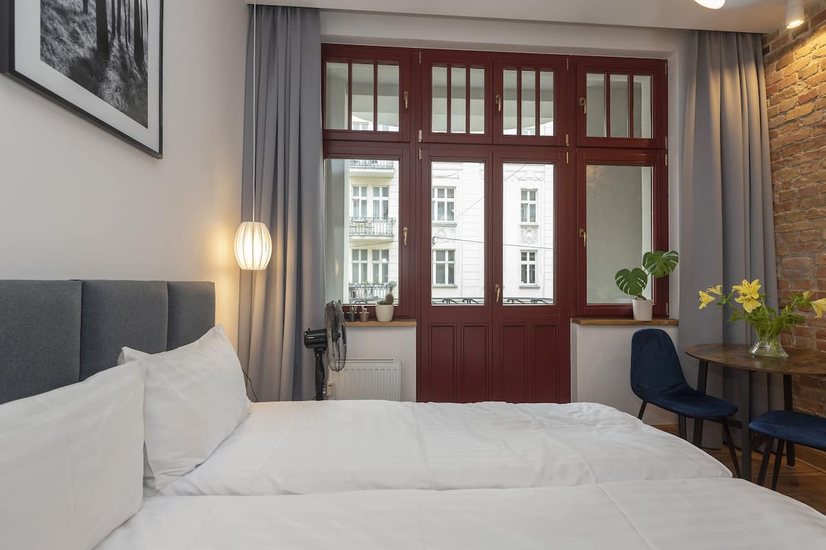 Une chambre d’hôtel comprenant un lit, un bureau avec une chaise, une fenêtre avec des rideaux et une vue sur les bâtiments environnants.