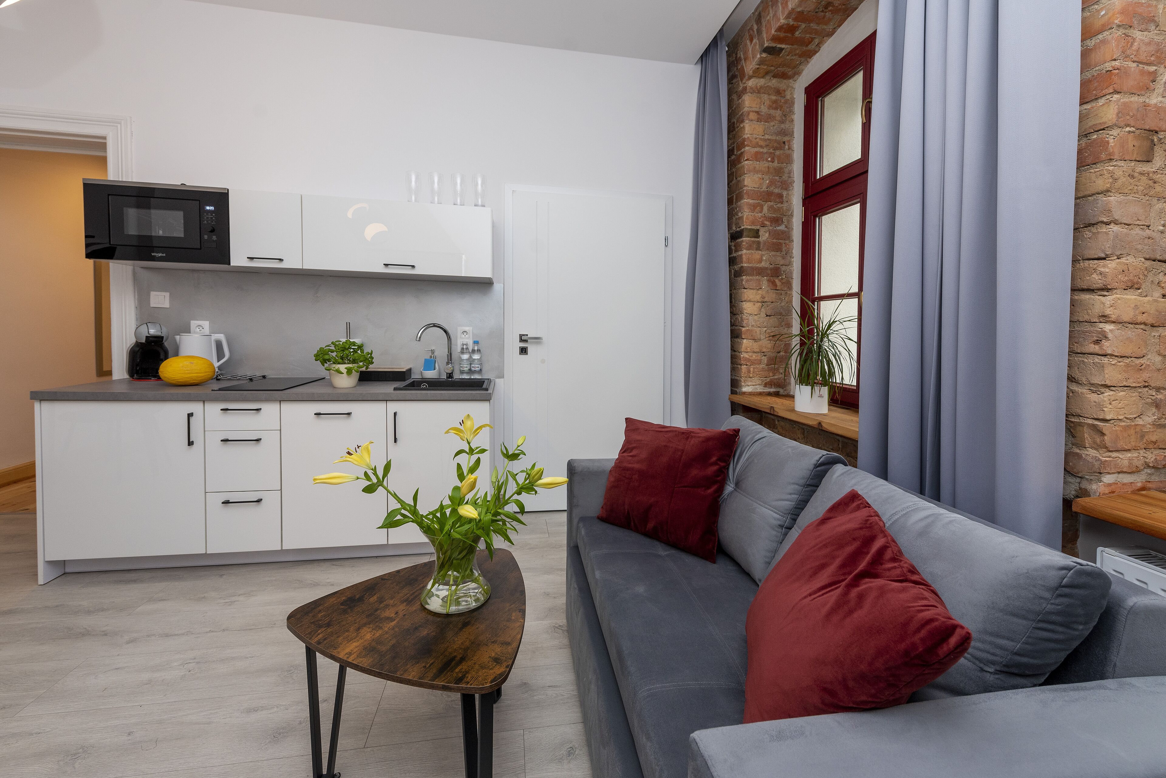 A modern living room with a grey sofa, red cushions, a wooden coffee table, and a vase with flowers.