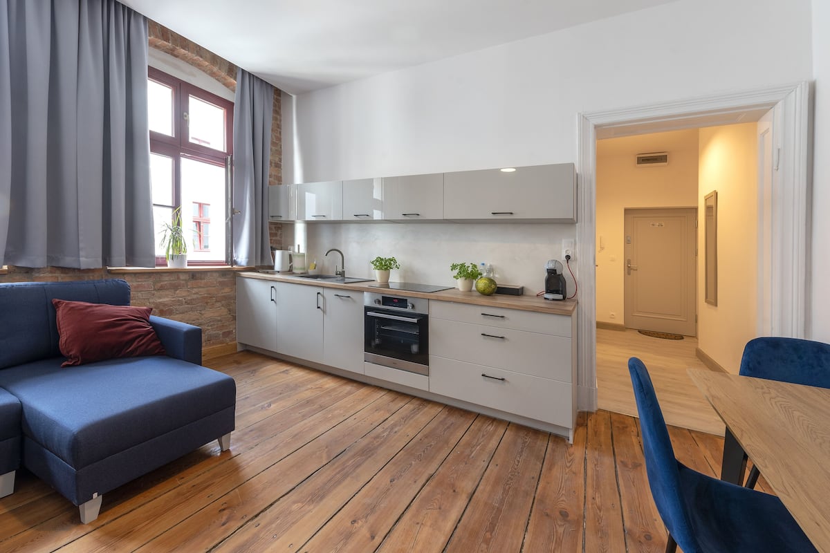 Eine moderne Küche mit weißen Schränken, einem Einbauofen und einem Essbereich mit Holztisch und blauen Stühlen.