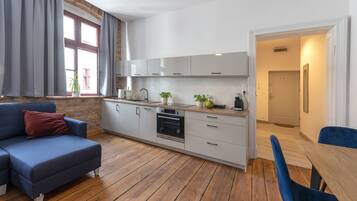 Eine moderne Küche mit weißen Schränken, einem Einbauofen und einem Essbereich mit Holztisch und blauen Stühlen.